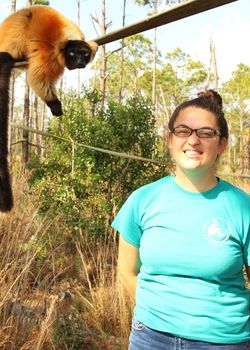 Meredith staff pic LCF Senior Keeper Meredith Hinton looks at camera with red ruffed lemur in background