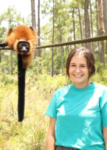 Keeper Madeline Larrison smiles at camera with lemur in background